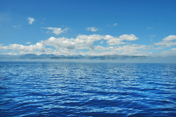 Obraz premium sea lanscape. blue sky, clouds over the surface of sea. mountain on horizon