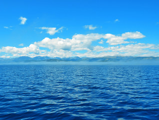 Fototapeta na wymiar sea lanscape. blue sky, clouds over the surface of sea. mountain on horizon