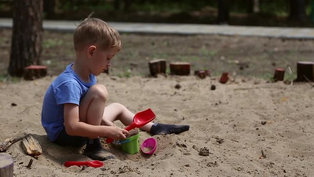 A boy plays in the sandbox with shovel and pail and shapes for sand
