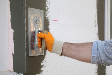 Worker spreading  mortar over styrofoam wall insulation with trowel