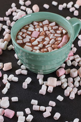 Hot chocolate in a green cup with marshmallows scattered around