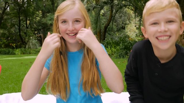 Blond boy and girl tickle each other and smile at the camera - slowmo