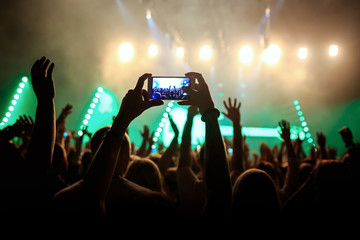 Rock concert crowd recording performance with digital smartphone, green guitar in stage