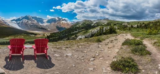 Fototapeta na wymiar Panorama Pair of Red Chairs on the Trail Up to Wilcox Pass