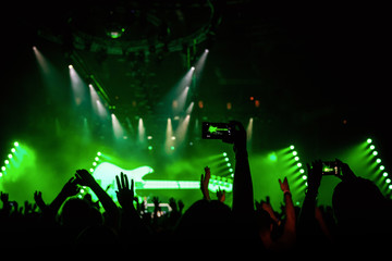 Rock concert crowd recording performance with digital smartphone, green guitar in stage