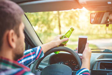 Drunk young man driving a car with a bottle of beer and mobile phone. Don't drink and drive...