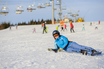 Young woman skier in blue ski suit lying on the snow at ski resort after the fall on mountain slope. Ski resort. Winter sports concept. Bukovel