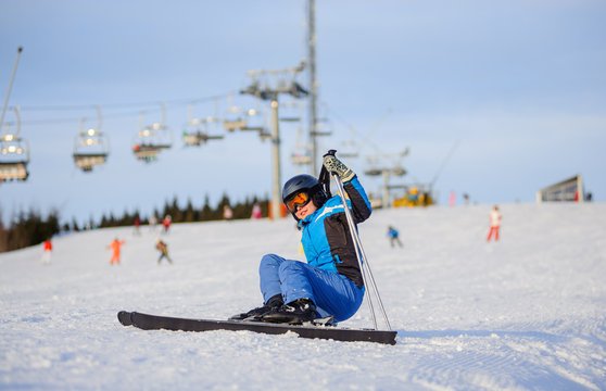 Young female skier in blue ski suit getting up after the fall on mountain slope against ski-lift. Ski resort. Winter sports concept.