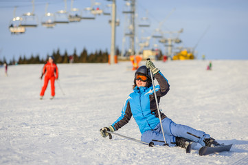 Fototapeta na wymiar Young woman skier in blue ski suit trying get up after the fall on mountain slope. Ski resort. Winter sports concept. Ski resort at Carpathian Mountains