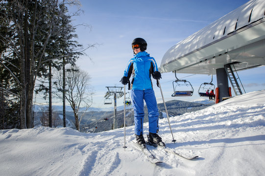Full length portrait of woman skier on the top of ski slope with ski-lift and mountains on the background on sunny day. Winter sports concept.