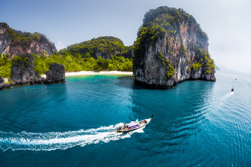 Aerial view of clear sea with traditional longtail thai boats and the rocky crag on the background