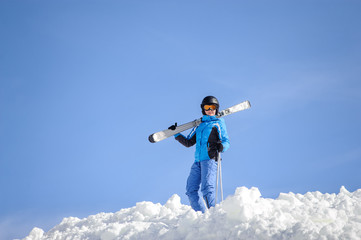 Fototapeta na wymiar Skier standing on top of the mountain against blue sky on a sunny day. Girl is holding skis on her shoulder smiling and looking into the camera. Winter sports concept. Carpathian Mountains