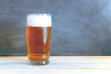 A glass of chilled beer on a white wooden table. Blackboard background composition with an empty copy space for Editor's text.