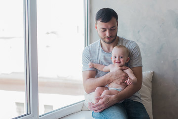 Portrait of young happy man holding his sweet baby. Young father embracing his baby with love and care, smiling. Indoors shot