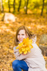 Naklejka na ściany i meble Young woman with autumn leaves in hand and fall yellow maple garden background