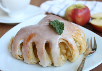 Apfeltasche auf einem Weißen Teller mit frischen Äpfeln und einer Tasse Kaffee im Hintergrund auf einem braunen Holztisch