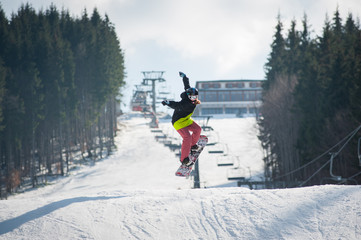 Female boarder on the snowboard jumping over the slope in winter with snowy slope and ski lifts in...