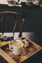 cooking ginger, lemon and honey hot tea in dark rustic interior. Ingredients and cup on wooden background