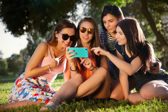 Summer outdoor portrait of three friends fun girls taking photos with a smartphone at bright sunset.