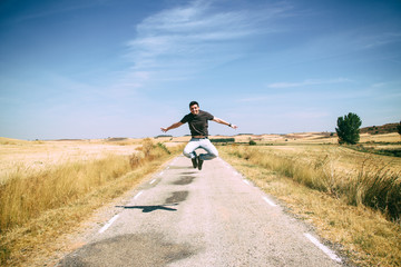 Chico joven saltando de alegría en una carretera vacía en medio del campo