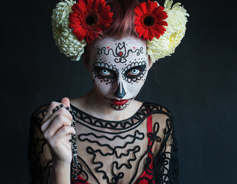 frightening photograph of a beautiful girl with a pattern on the face and red flowers in her hair Los Muertos