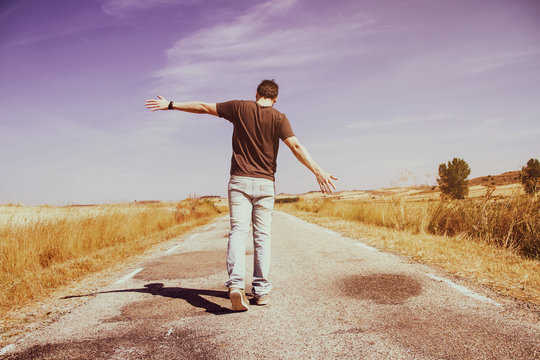 Hombre joven caminando por una carretera vac&iacute;a 