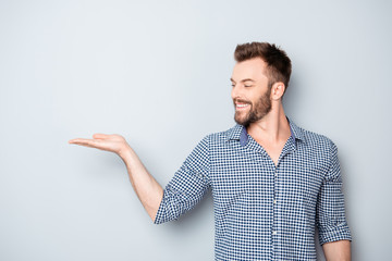 Portrait of young man showing product isolated on gray backgroun