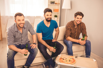 Portrait of handsome friends sitting on sofa with beer and pizza