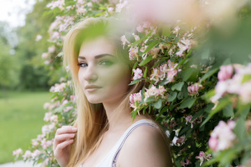 Fototapeta premium beautiful lovely girl with long blonde hair enjoying nature near blooming rosebush in a white t-shirt with full lips bright summer day