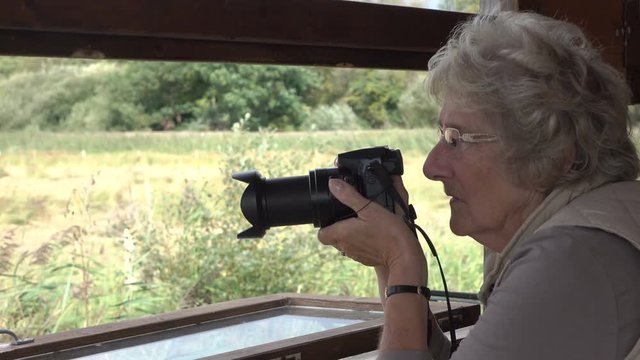 Senior woman with camera takes picture in bird hide