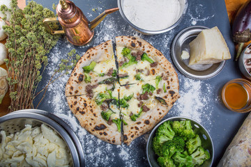 Traditional italian pizza with mozzarella, broccoli and salsiccia, on a black stone with the ingredients