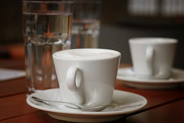 White cup of coffee and glasses of water on the wooden table