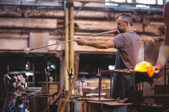 Glassblower shaping glass on blowpipe in factory