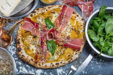 Traditional italian pizza with pumpkin pesto, ham, gorgonzola and seeds on black chalkboard