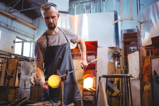 Glassblower shaping molten glass in workshop