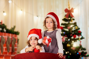 Sisters twins child in Christmas hats Santa with gifts near the