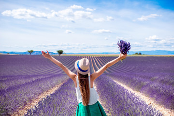 Young woman with raised hands holding lavender bouquet standing on the lavender field in Provence