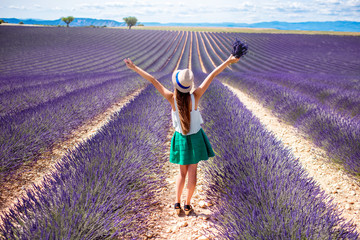 Young woman with raised hands holding lavender bouquet standing on the lavender field in Provence