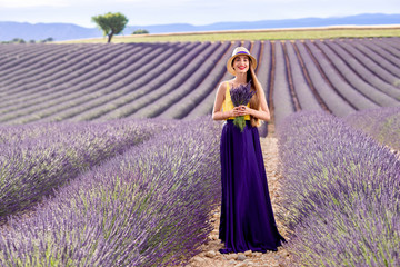 Young pretty woman in the long violet skirt standing with lavender bouquet on the lavender field in Provence in France
