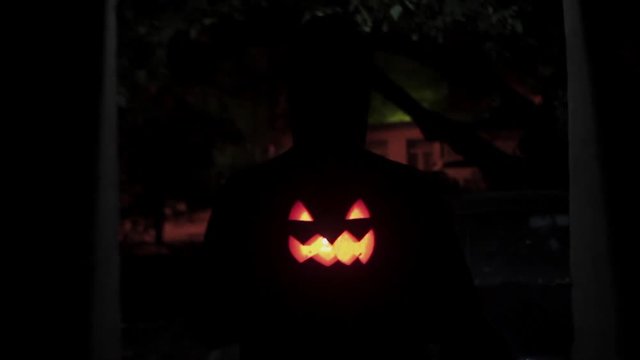 Black silhouette figure carries jack o lantern carved pumpkin through dark alley
