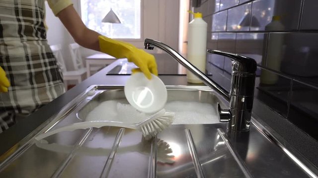 The housewife washes the dishes in the sink in the kitchen. Slow Motion. Dolly shot.