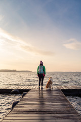 Fototapeta premium Woman with dog enjoy sunrise at lake, backpacker looking at beautiful morning view