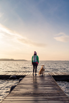 Woman with dog enjoy sunrise at lake, backpacker looking at beautiful morning view