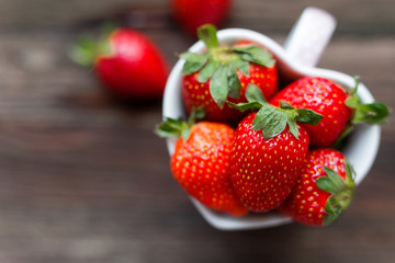 Fresh juicy strawberries in cup shaped as a heart, symbol of love. Rustic wooden background. Top view, place for text.