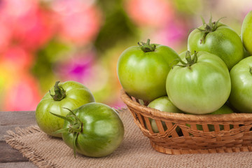 unripe green tomatoes in a wicker basket on wooden table with blurred background