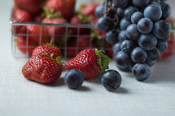 Strawberries and grapes in a small basket on a metal table.