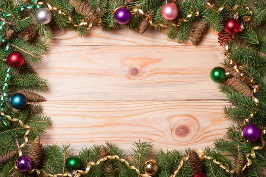 frame of fir branches with Christmas decorations on a light wooden background