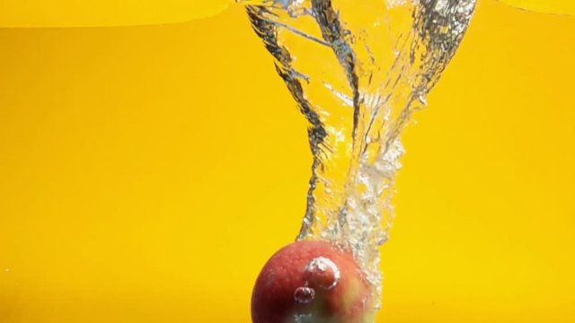 one red apple falling underwater against yellow background in slow motion.
