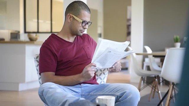 Portrait of hispanic guy reading newspaper at home