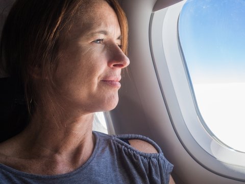 Woman is looking through a window in the aircraft. .